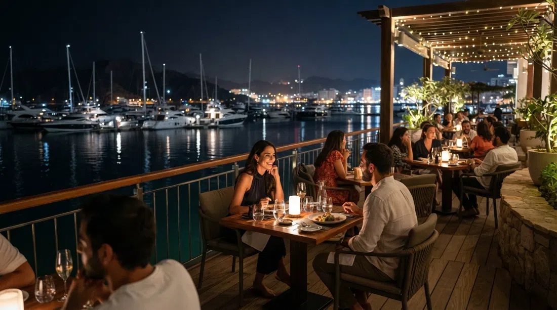 la terraza de Huqqa junto a la marina de noche, mesas iluminadas sobre el agua con yates y reflejos al fondo